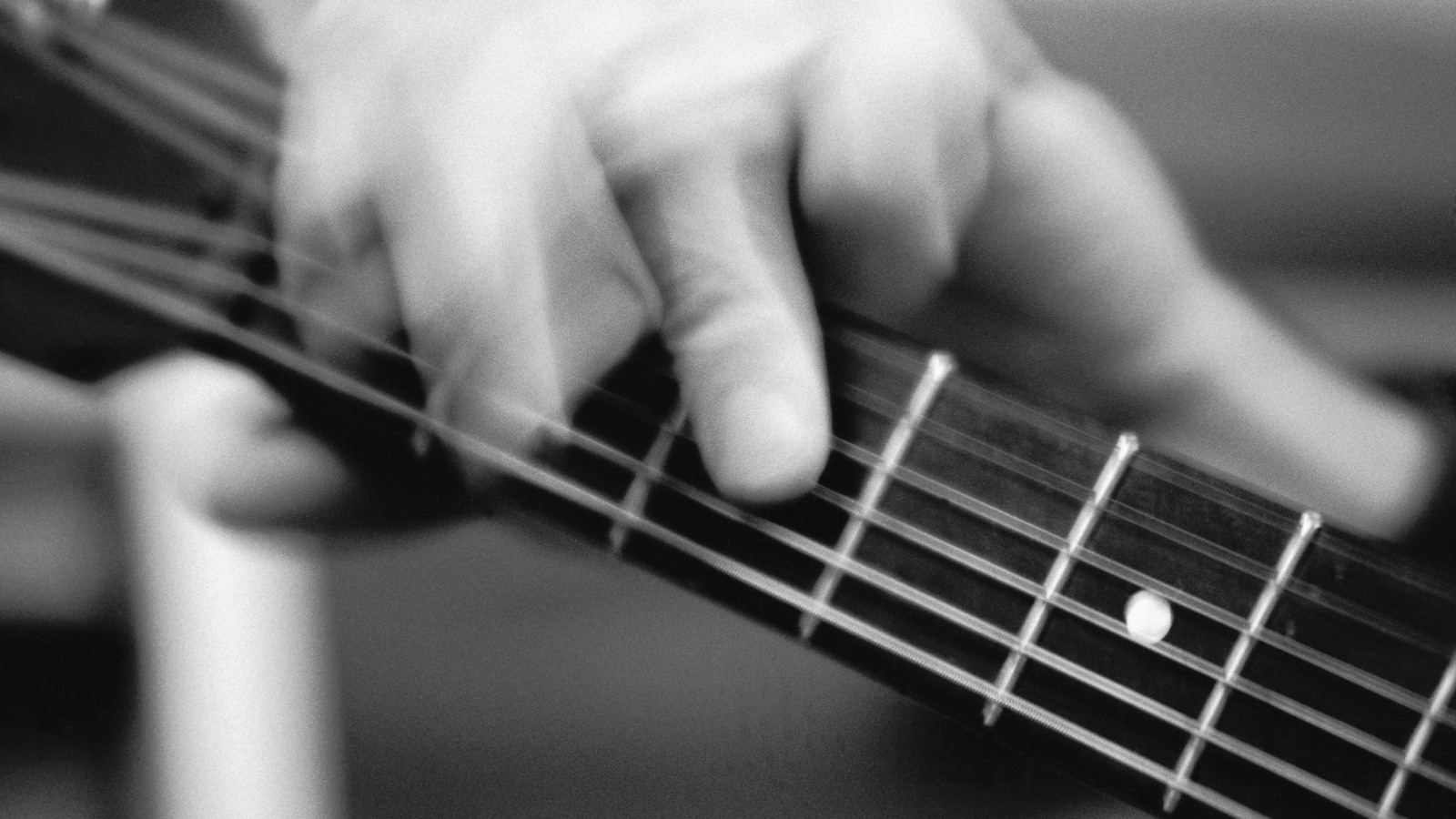 En svartvit bild som visar halsen på en gitarr och fingrar som spelar