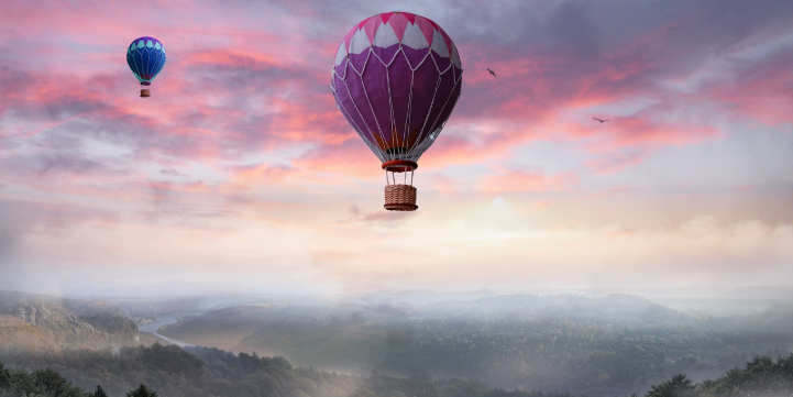 Två varmluftsballonger svävar över ett dimhöljt landskap i soluppgångens rosa och lila ljus. Bilden förmedlar känslan av ett äventyr i en fantasivärld.