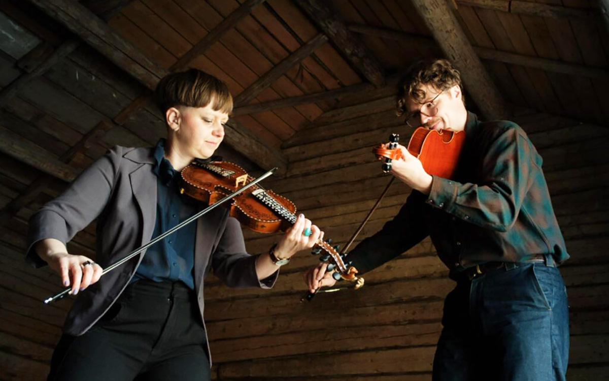 Fyra personer står i en skogsdunge och håller olika instrument: saxofon, kontrabas, fiol och trumma.