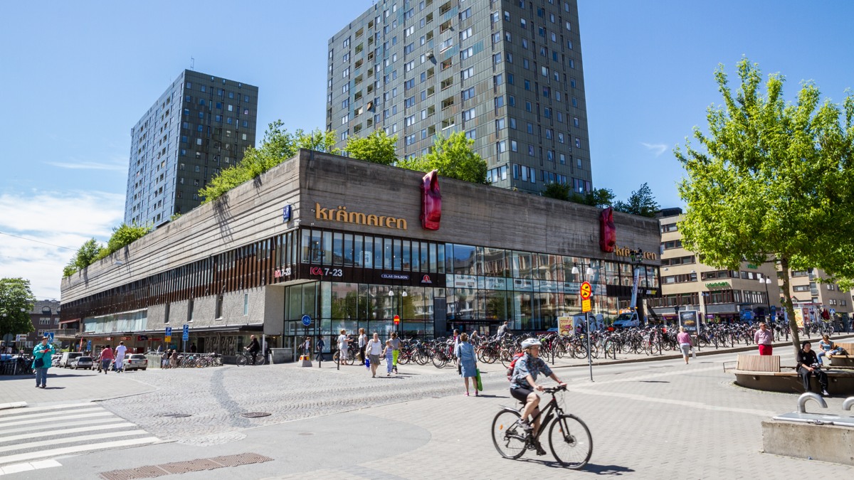 En man cyklar längs en gata bredvid höga byggnader.