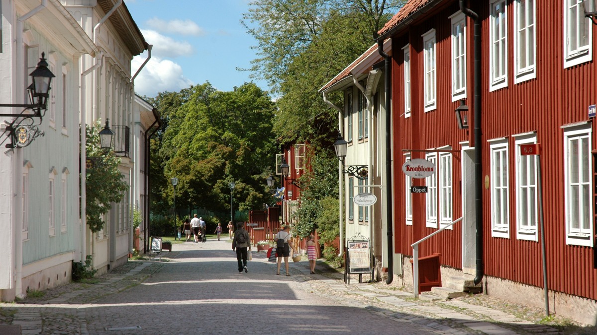 Två personer går längs en gata bredvid en röd byggnad.