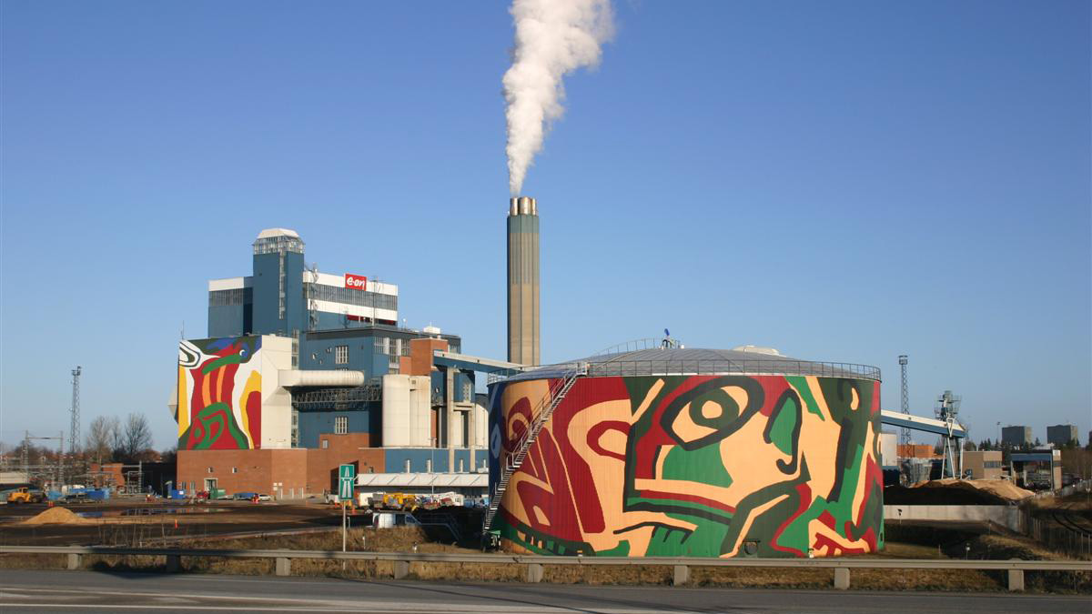 EONs anläggning med en stor färgglad silo dekorerad med abstrakt konst och en hög skorsten som släpper ut vit rök mot en klar blå himmel.