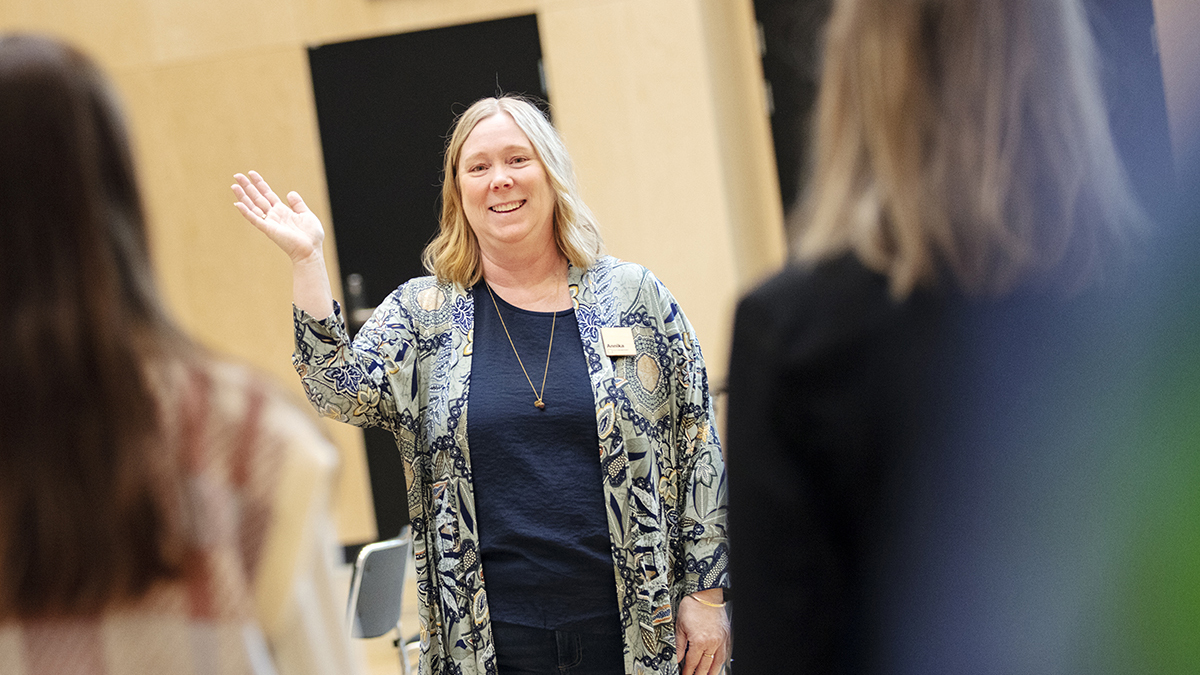 Blond kvinna som gestikulerar inför några åskådare