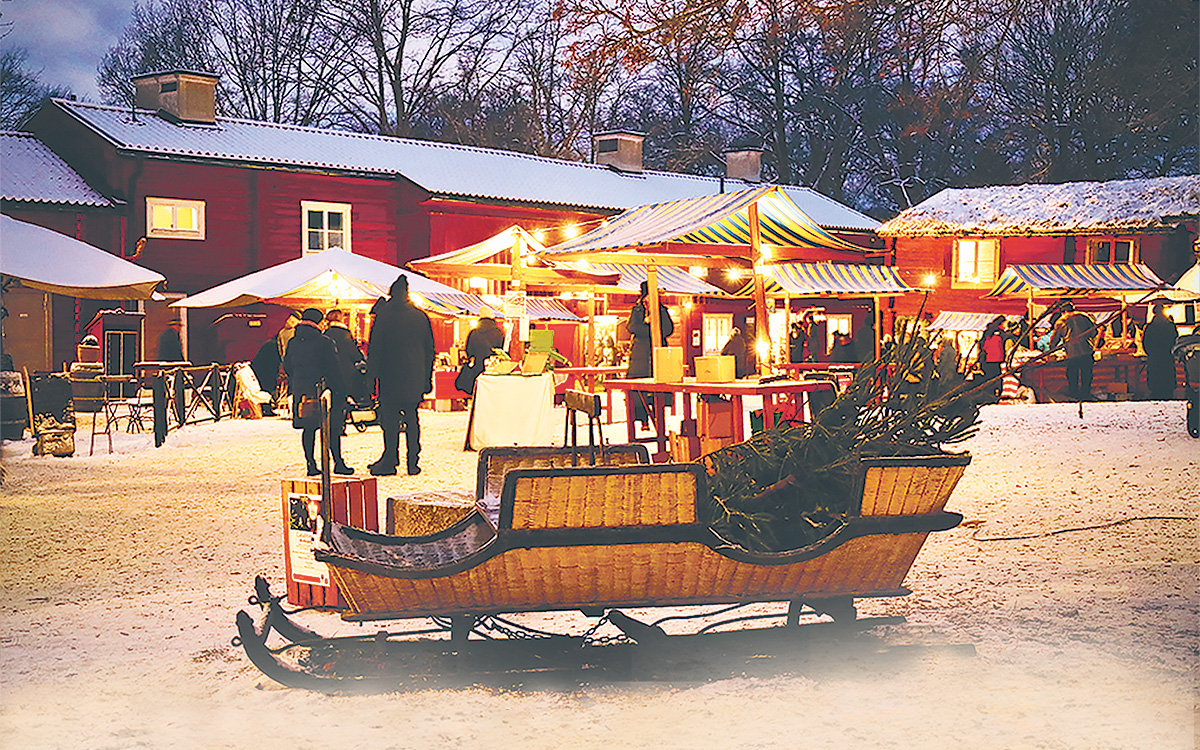 En släde framför röda hus, snön ligger vit på marken.
