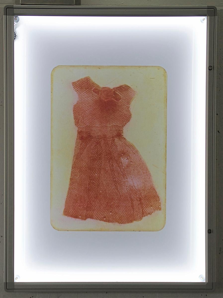 Inramat hänger ett grafiskt tryck på en röd klänning som tryckts på en plåt. 