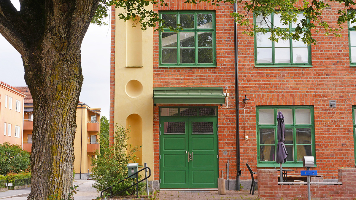 Grön port i tegelhus. I förgrunden syns ett träd.