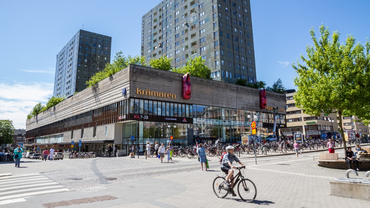 En man cyklar längs en gata bredvid höga byggnader.