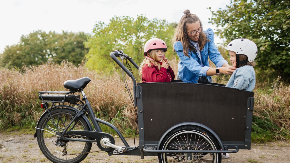 En kvinna med två barn i en lådcykel.