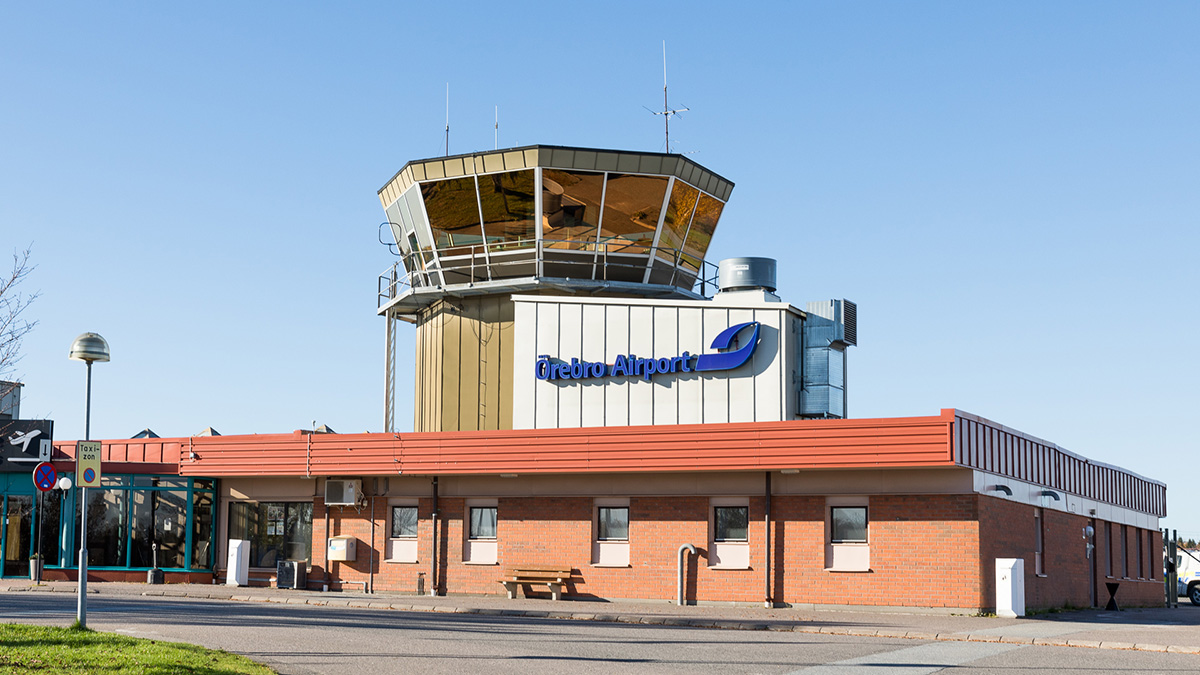Flygplatsbyggnad med kontrolltorn och skylten 'Örebro Airport' på fasaden, under klar blå himmel.
