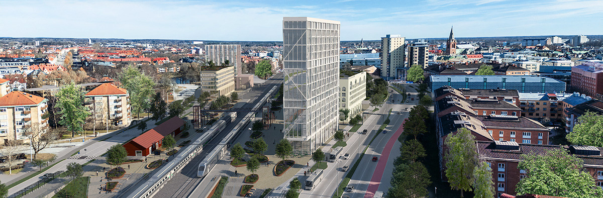 Perspektivisk visualisering över ett stadsområde med järnväg och station i mitten. I förgrunden syns spår med tåg, plattformar och en mindre stationsbyggnad i rött. Runt stationen har nya byggnader lagts in, bland annat ett högt, smalt höghus i glas samt flera mellanhöga kvarter. Gator med biltrafik, cykelbanor och trädplanterade gångstråk omger området. I bakgrunden breder stadens bebyggelse ut sig med kvarter, parker och kyrktorn i horisonten. Visualiseringen visar hur området kan utvecklas till en tätare stadsmiljö kring kollektivtrafiknoden.