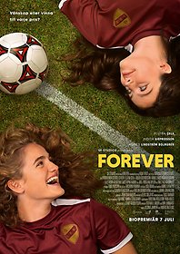 Två tjejer ligger på en fotbollsplan i vinröda tröjor och tittar på varandra och ler.